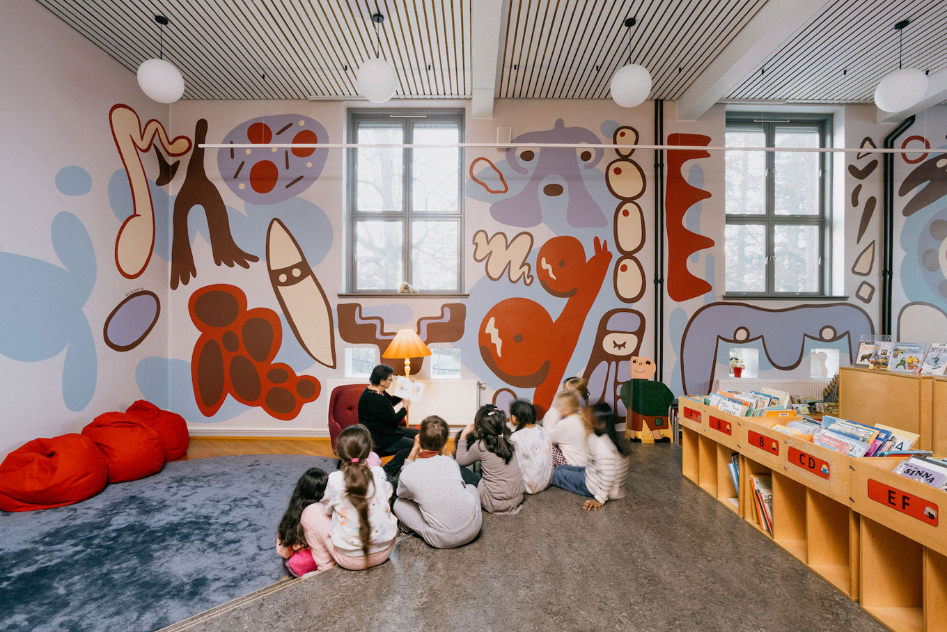 en gruppe barn som sitter i et rom med et stort veggmaleri