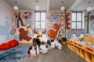 en gruppe barn som sitter i et rom med et stort veggmaleri
