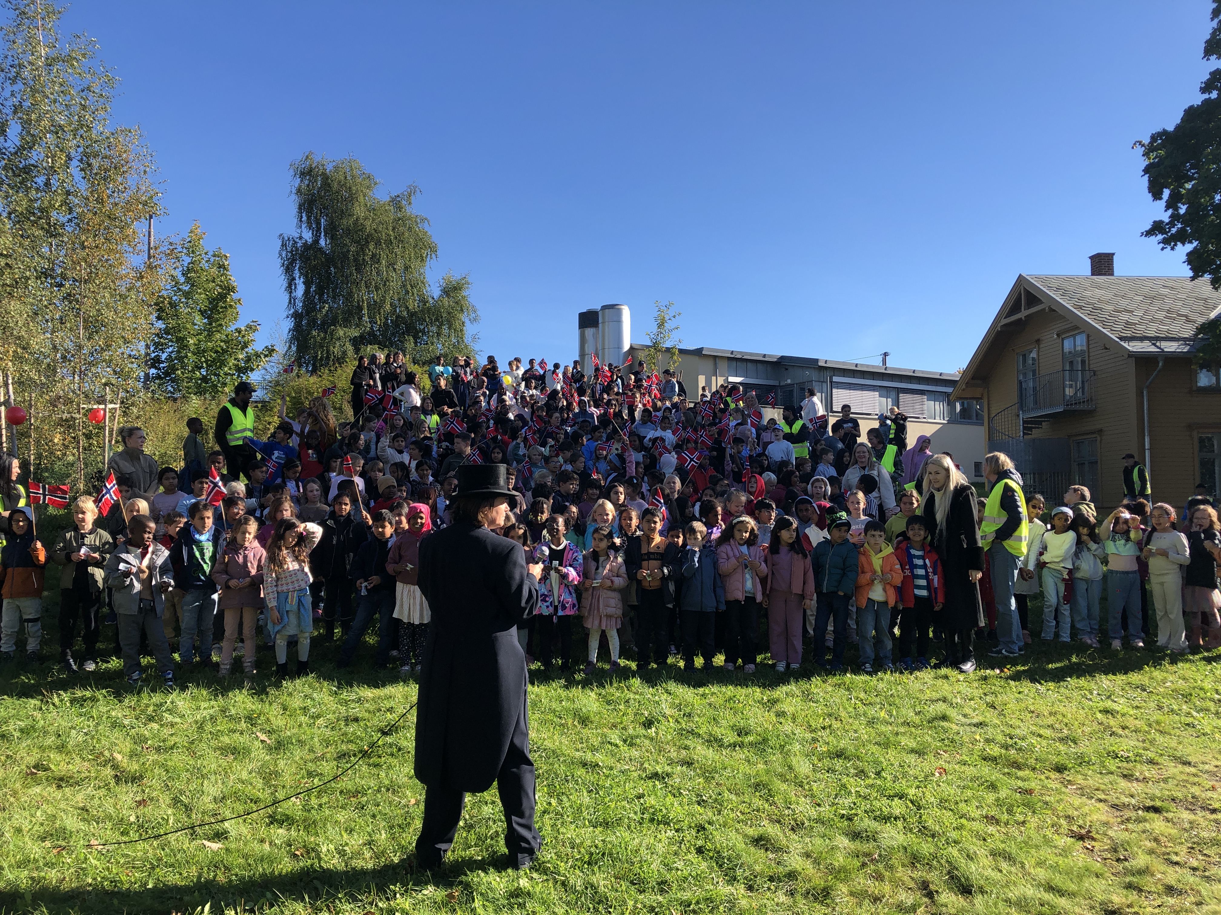en person i konfirmasjonslue og kjole som står foran en stor gruppe mennesker