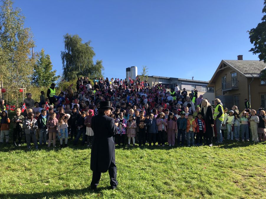 en person i konfirmasjonslue og kjole som står foran en stor gruppe mennesker